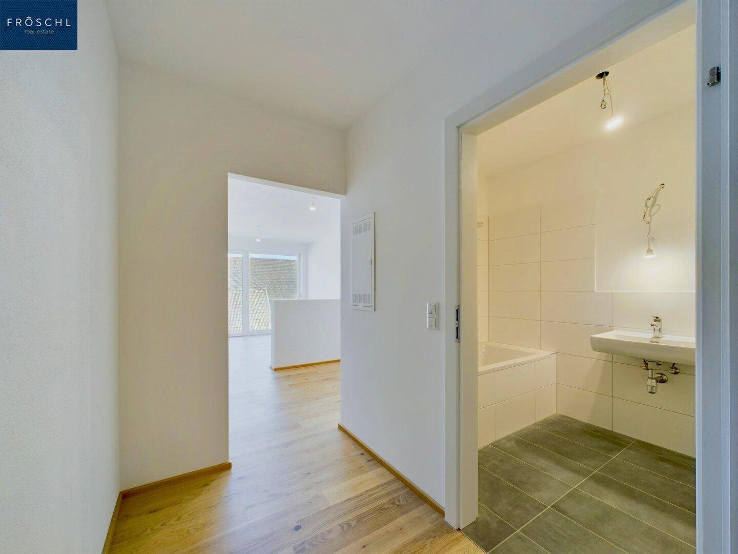 Heller Flur mit Holzboden, der zu einem Badezimmer und weiteren Räumen führt.