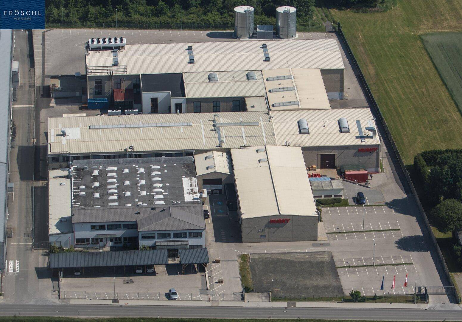 Luftaufnahme des weitläufigen Gewerbeareals mit mehreren Gebäuden und umliegenden Feldern.