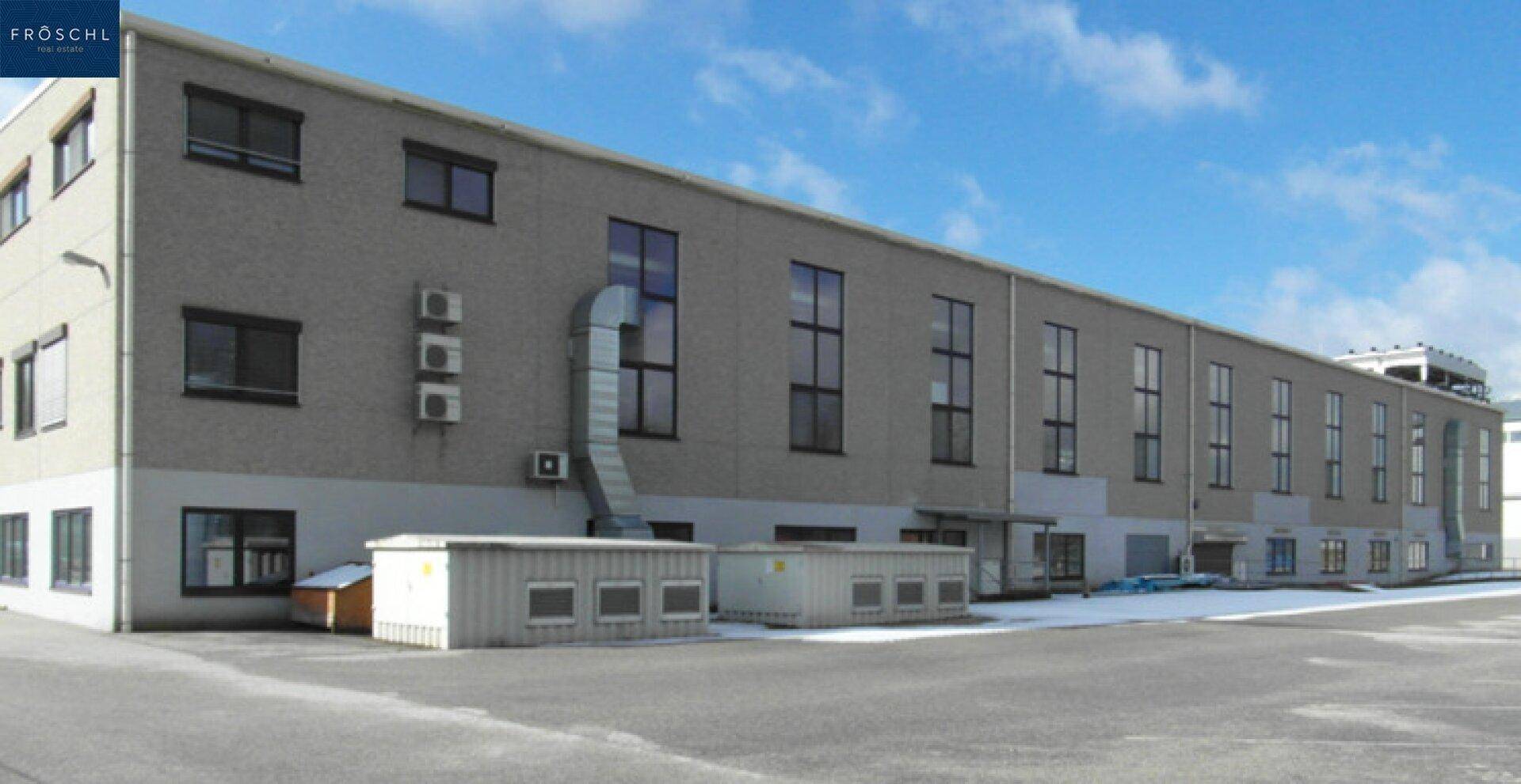 Fassade eines großen Industriegebäudes mit vielen Fenstern und externen Lüftungsanlagen.