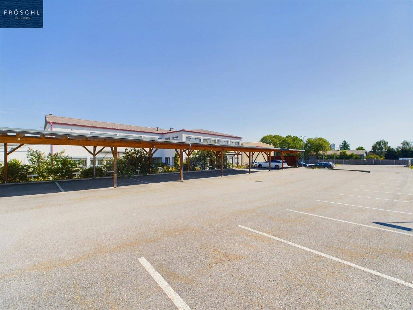 Weitläufiger Parkplatz mit zahlreichen Stellplätzen und überdachten Carports im Hintergrund.