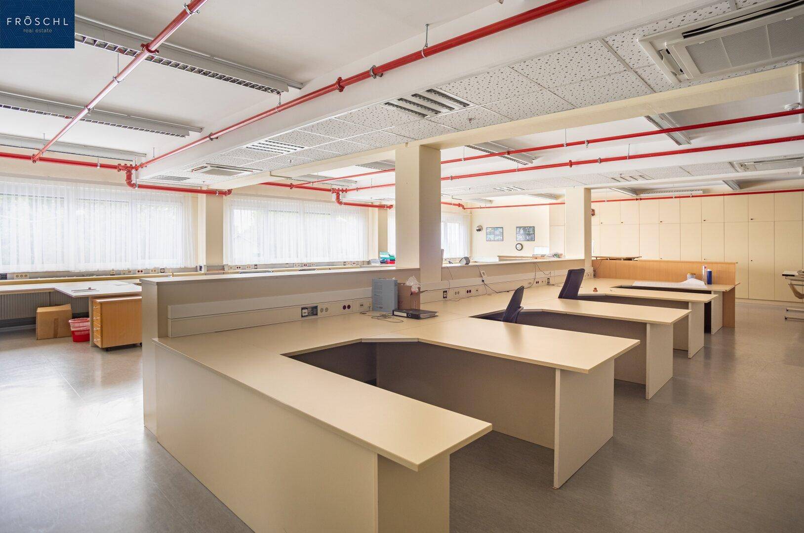 Geräumiges Büro oder Labor mit langen Arbeitsflächen, sichtbaren roten Rohren und Fenstern.
