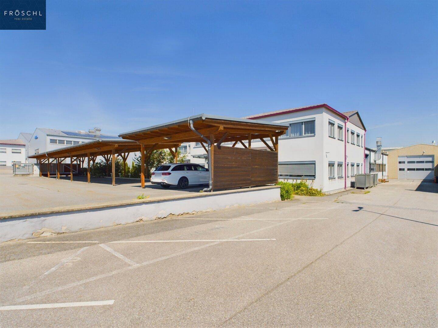 Außenbereich eines Anwesens mit einem weißen Gebäude und mehreren Holz-Carports sowie Parkplätzen.
