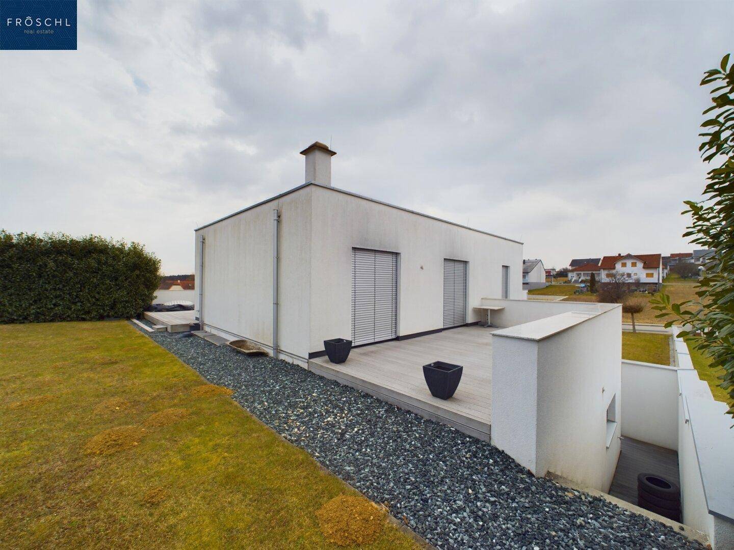 Moderne Hausfassade mit Flachdach und angrenzendem Gartenbereich mit Kiesweg.