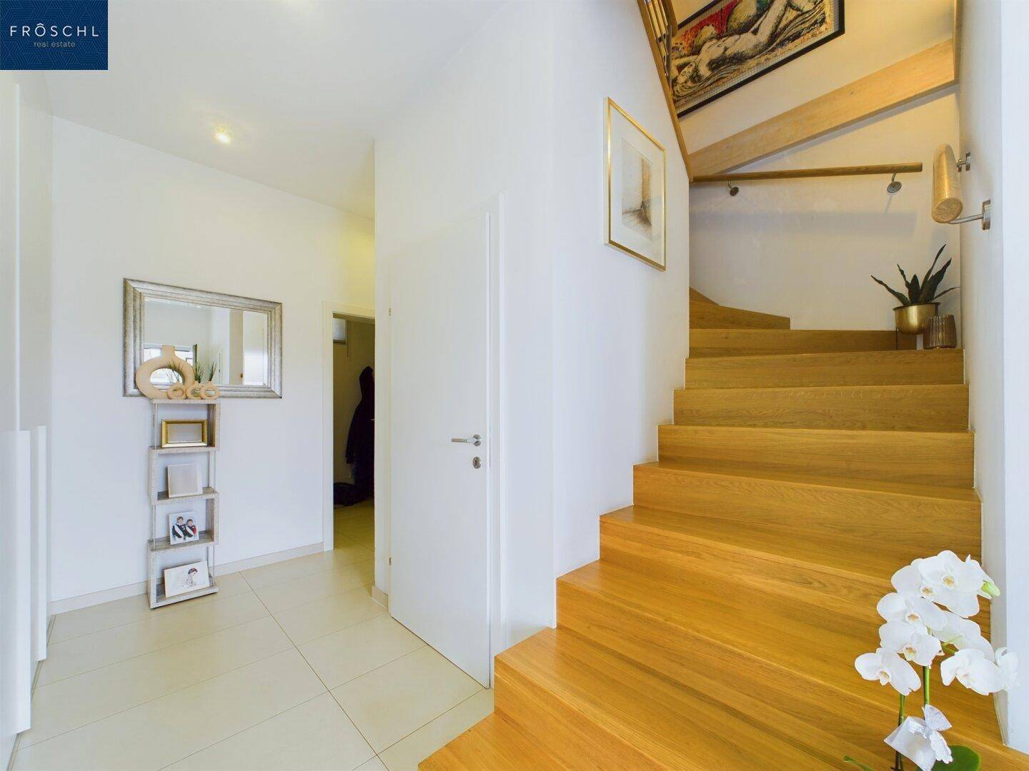 Geräumiger Flur mit eleganter Holztreppe und Spiegel, der zum Obergeschoss führt.
