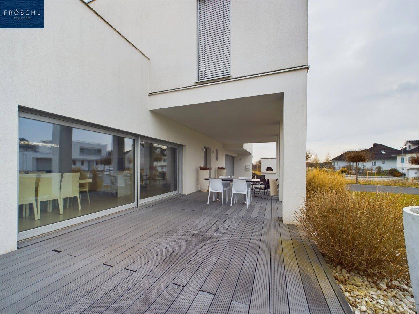 Geräumige Terrasse mit Holzboden und Blick auf die umliegende Landschaft und das Gebäude.