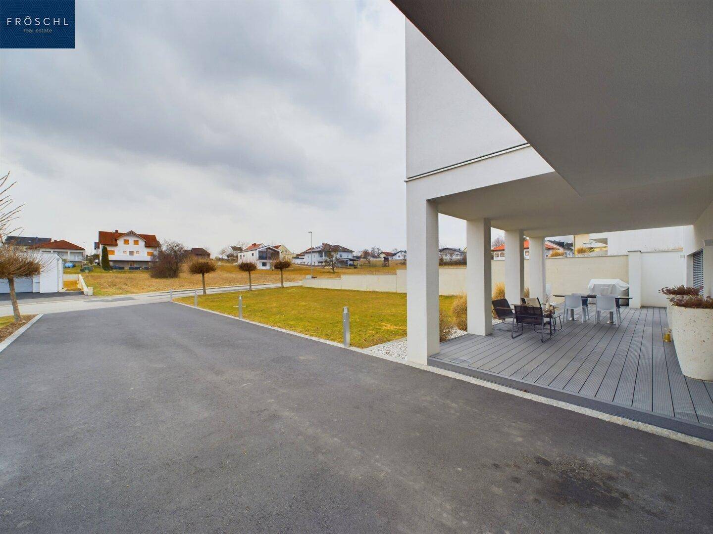 Zufahrt zum Haus mit angrenzender überdachter Terrasse und Blick auf die Umgebung.