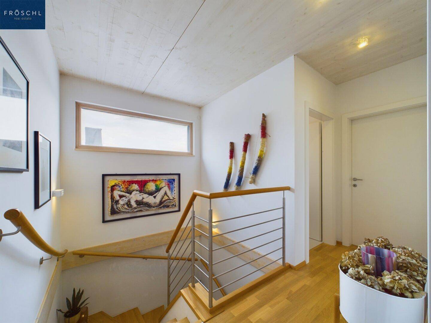 Treppenhaus mit Holzstufen und modernem Geländer, beleuchtet durch ein schmales Fenster.