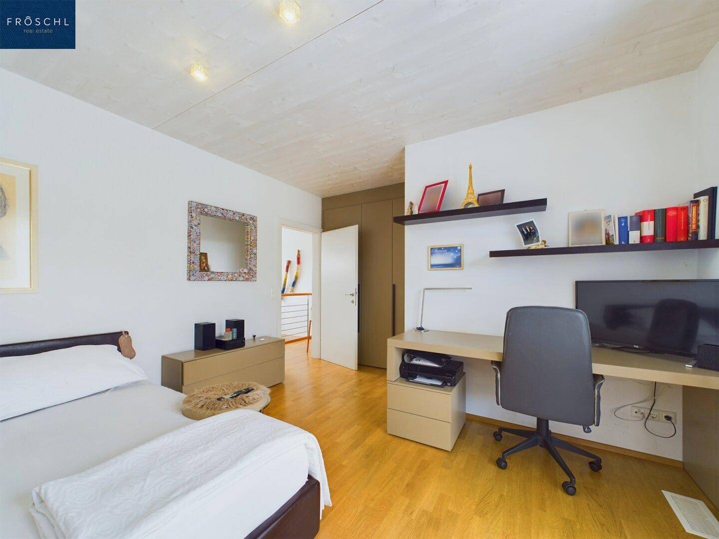 Schlafzimmer mit Arbeitsbereich, Holzboden und Blick auf die Umgebung durch das Fenster.
