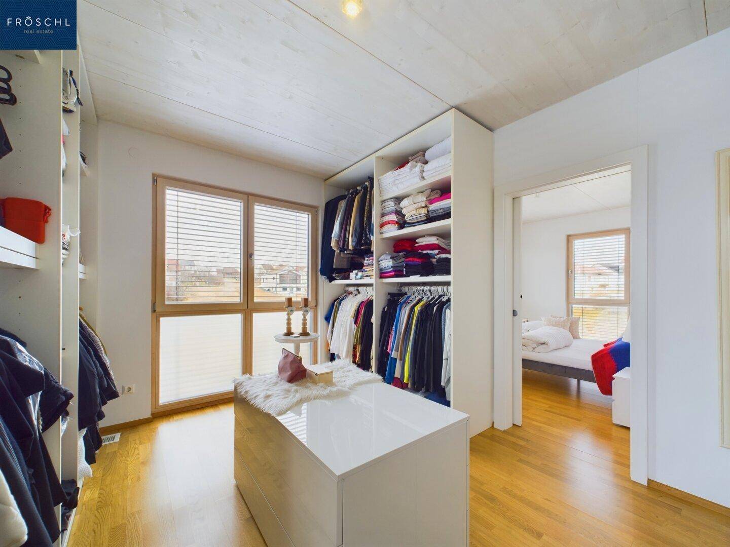 Geräumiger begehbarer Kleiderschrank mit viel Stauraum und Fenster für Tageslicht.