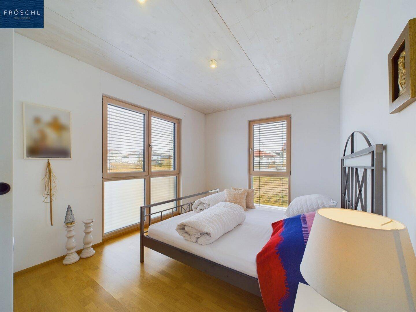 Gemütliches Schlafzimmer mit Holzboden und zwei Fenstern, die viel Licht hereinlassen.