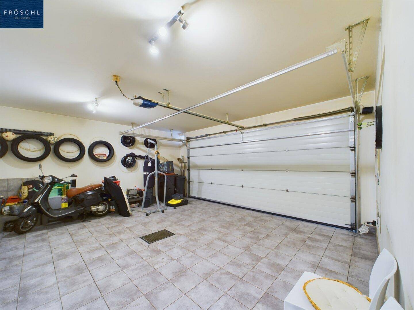Geräumige Garage mit Fliesenboden und automatischem Tor, bietet Platz für Fahrzeuge und Lagerung.