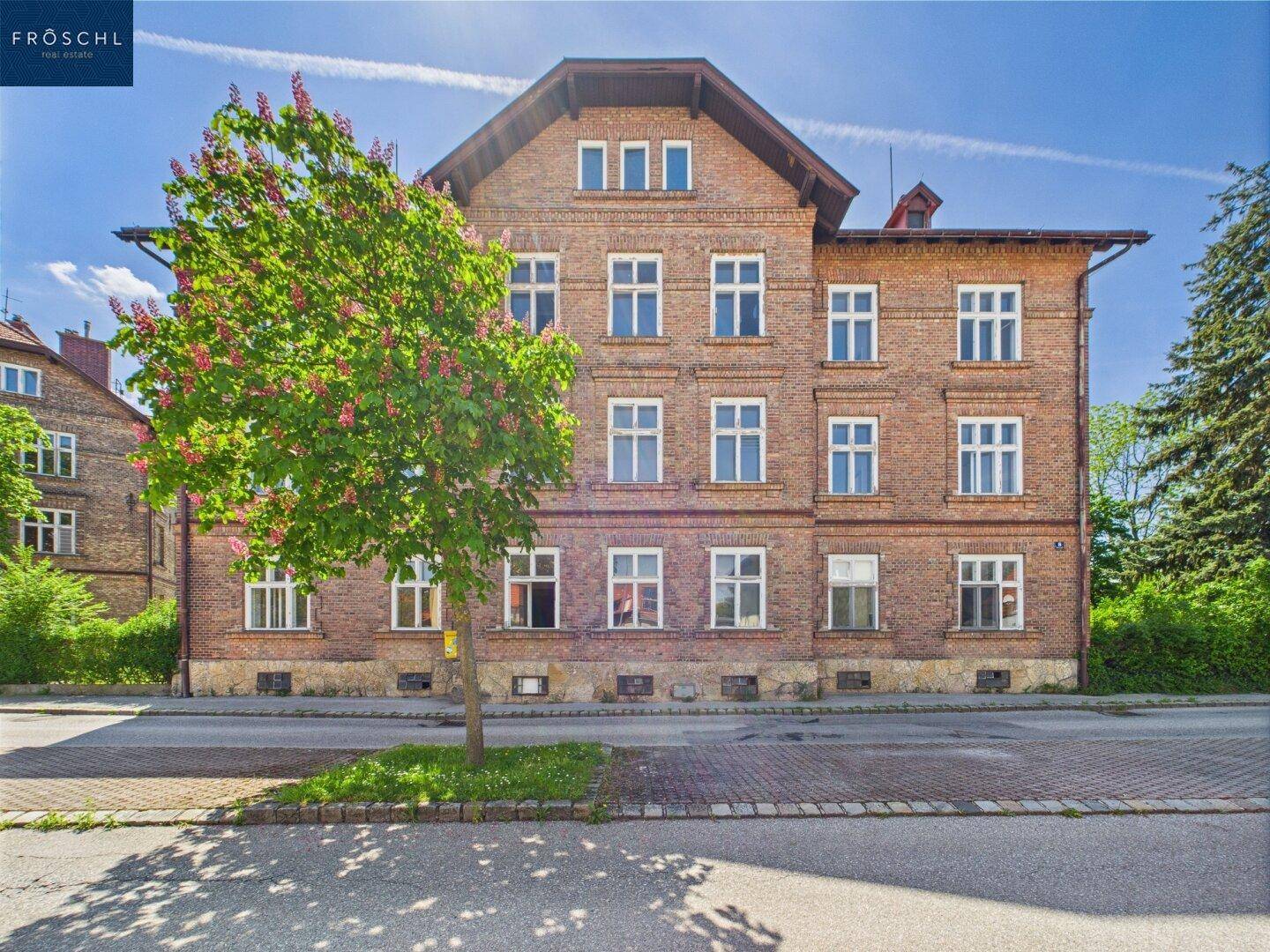 Historisches Ziegelgebäude mit blühendem Baum davor und traditioneller Fassadengestaltung.