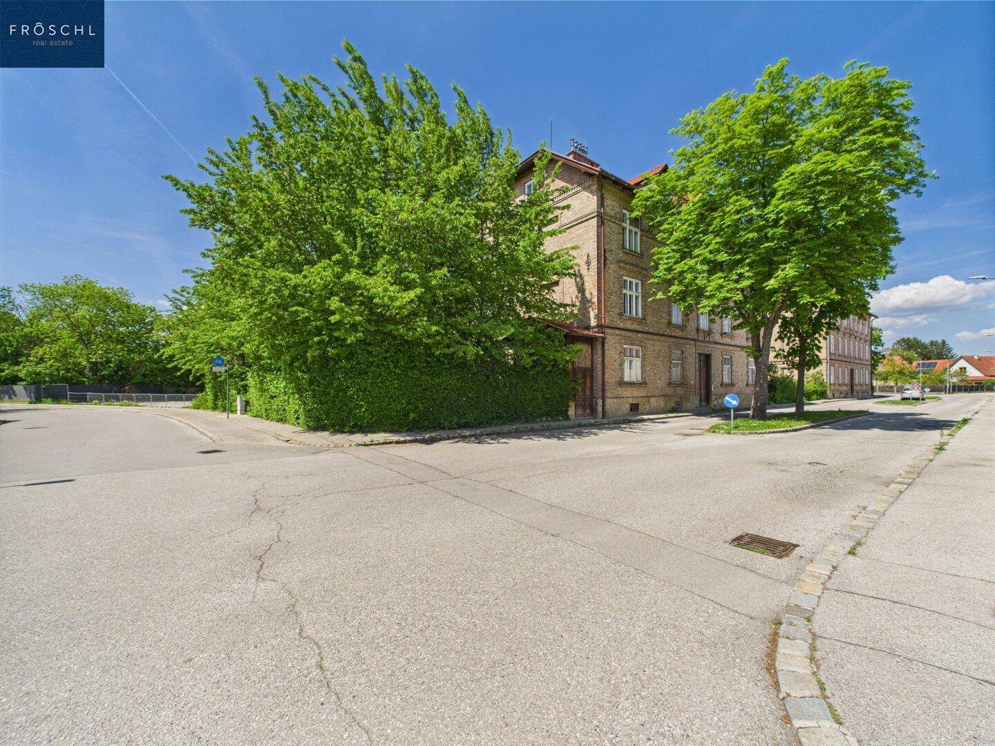 Historisches Ziegelgebäude hinter einem großen, grünen Baum an einer Straßenecke.
