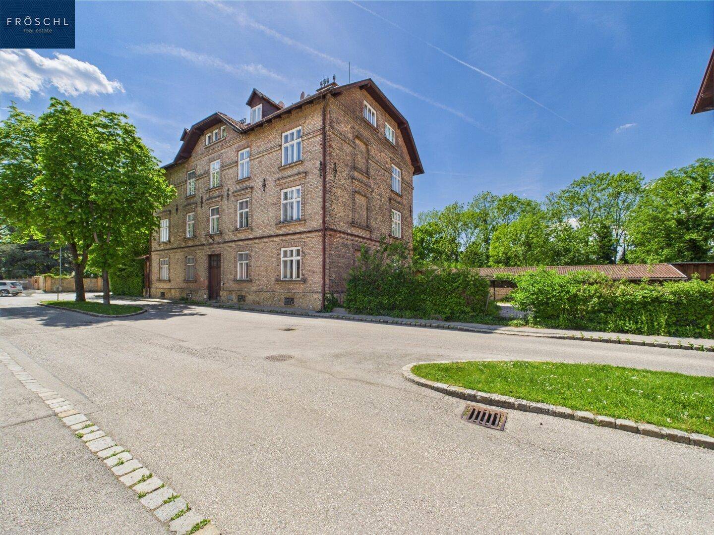 Eckansicht eines historischen Ziegelgebäudes an einer ruhigen Straße mit viel Grün.