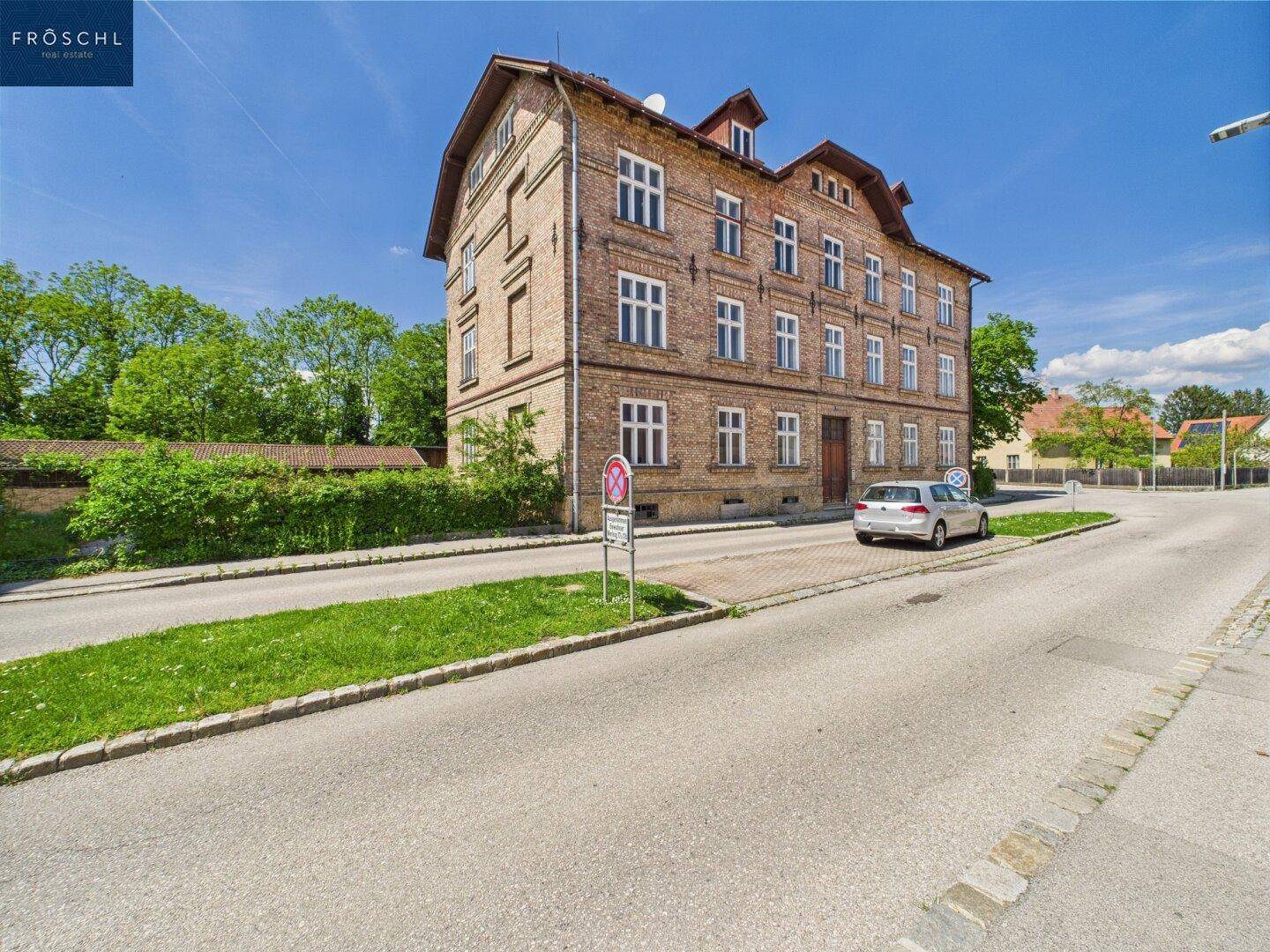 Historisches Backsteingebäude mit Mansarddach und gepflegter Grünfläche an der Straßenseite.