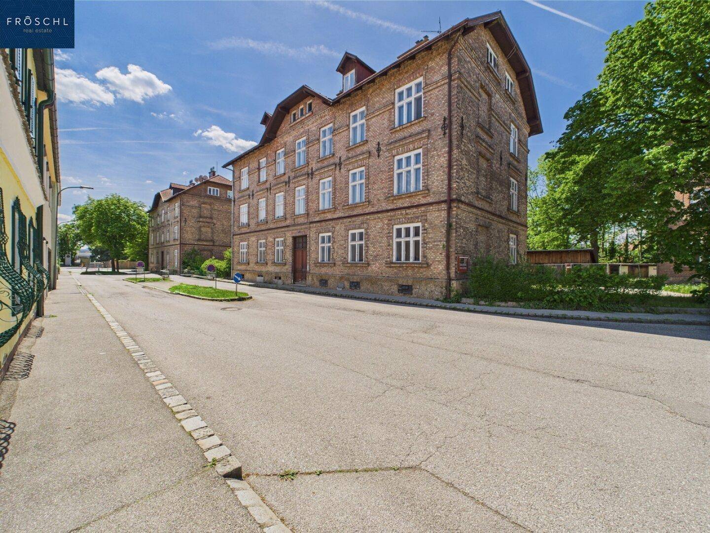 Seitenansicht eines historischen Backsteingebäudes an einer ruhigen Straße unter blauem Himmel.