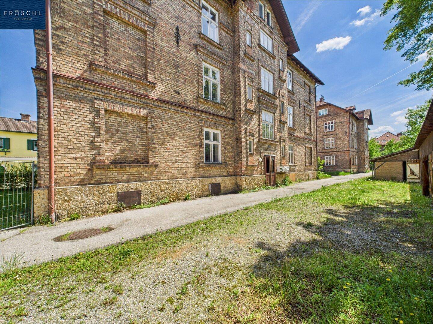 Seitenansicht eines Backsteingebäudes mit einem unbefestigten Weg und Grasflächen daneben.