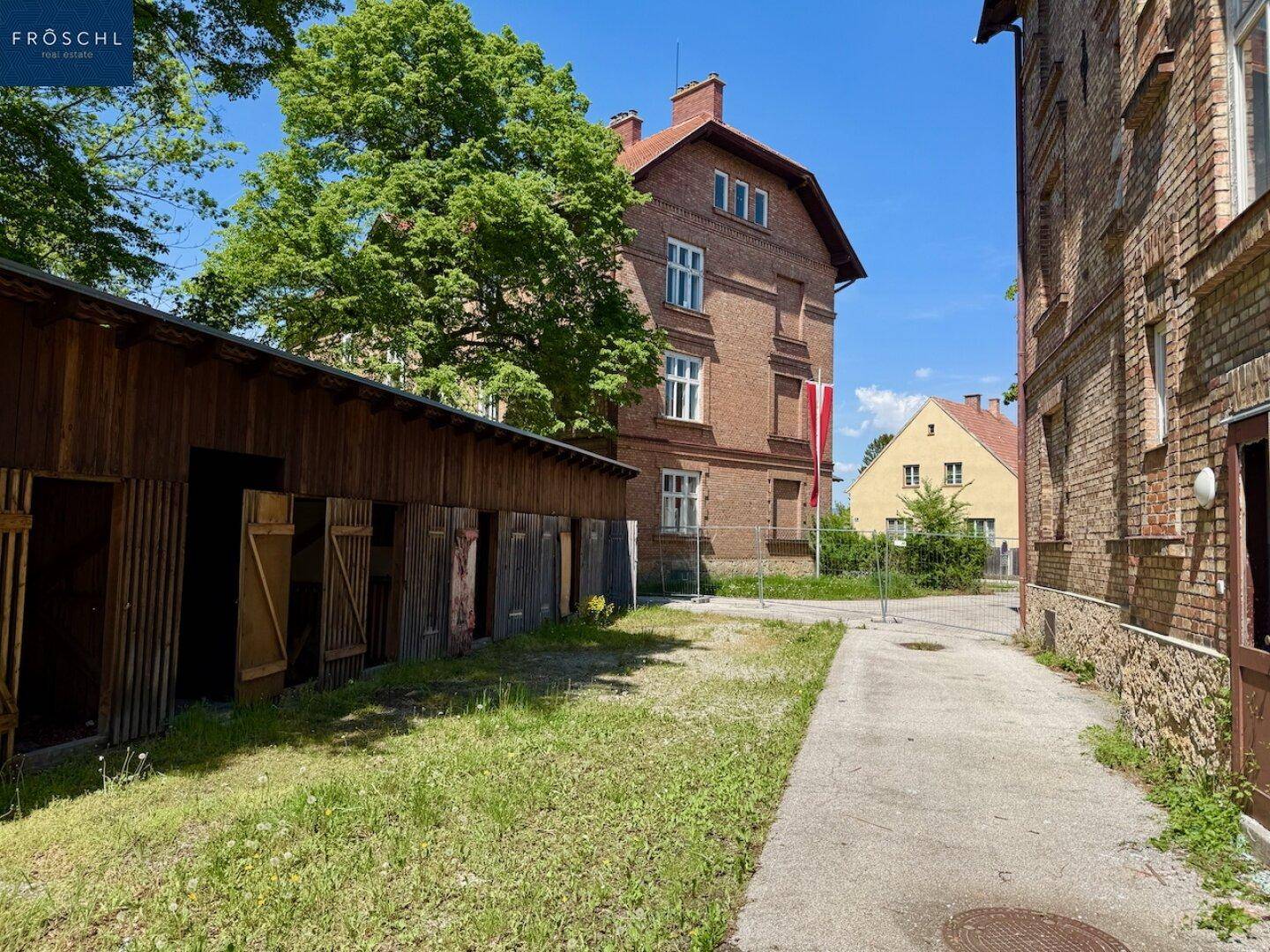 Rückseite eines Backsteingebäudes mit einem Holzschuppen und einer großen Grasfläche.