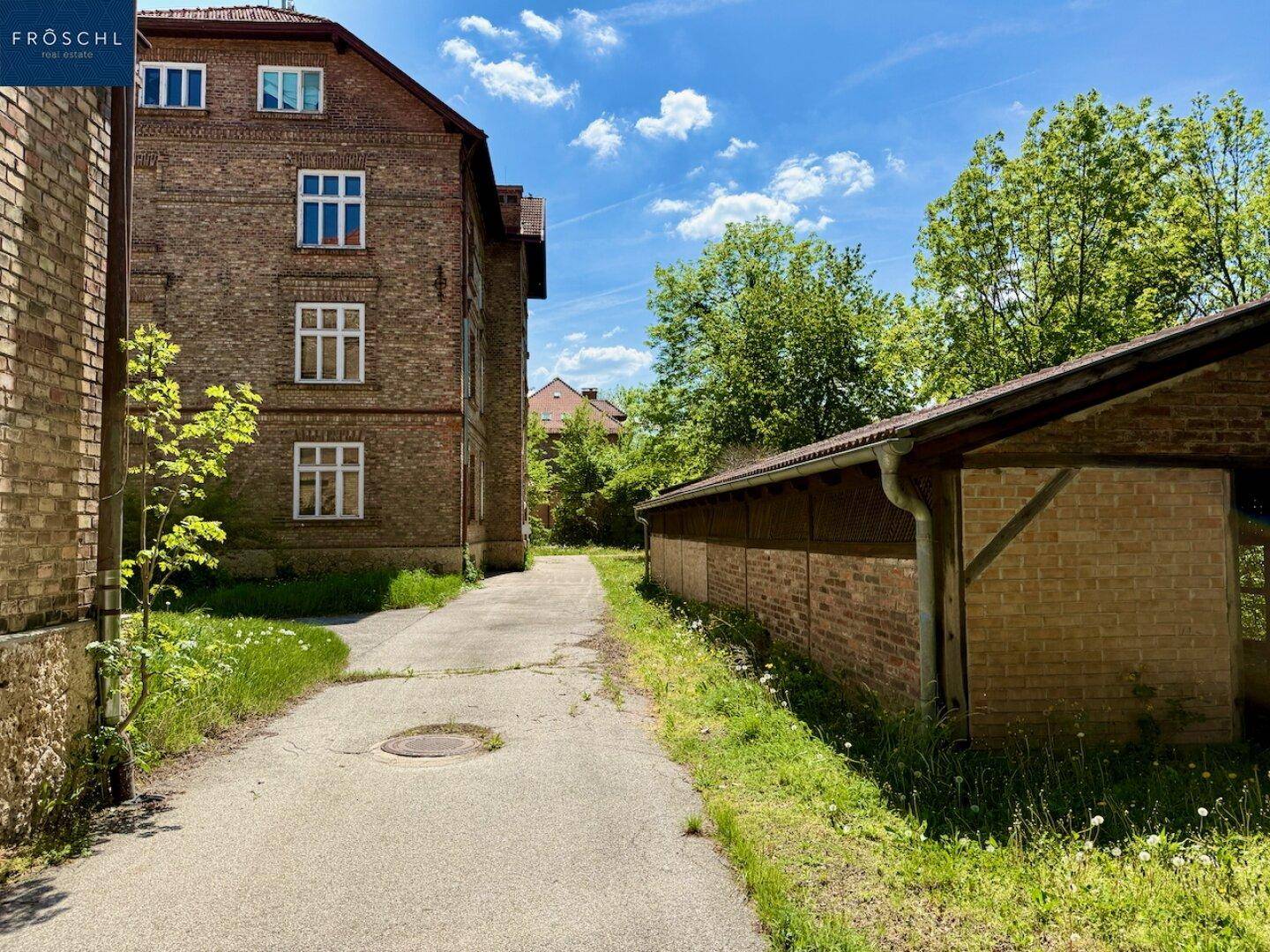 Seitenansicht des Gebäudes mit einem langen Schuppen oder Carport und einem unbefestigten Weg.