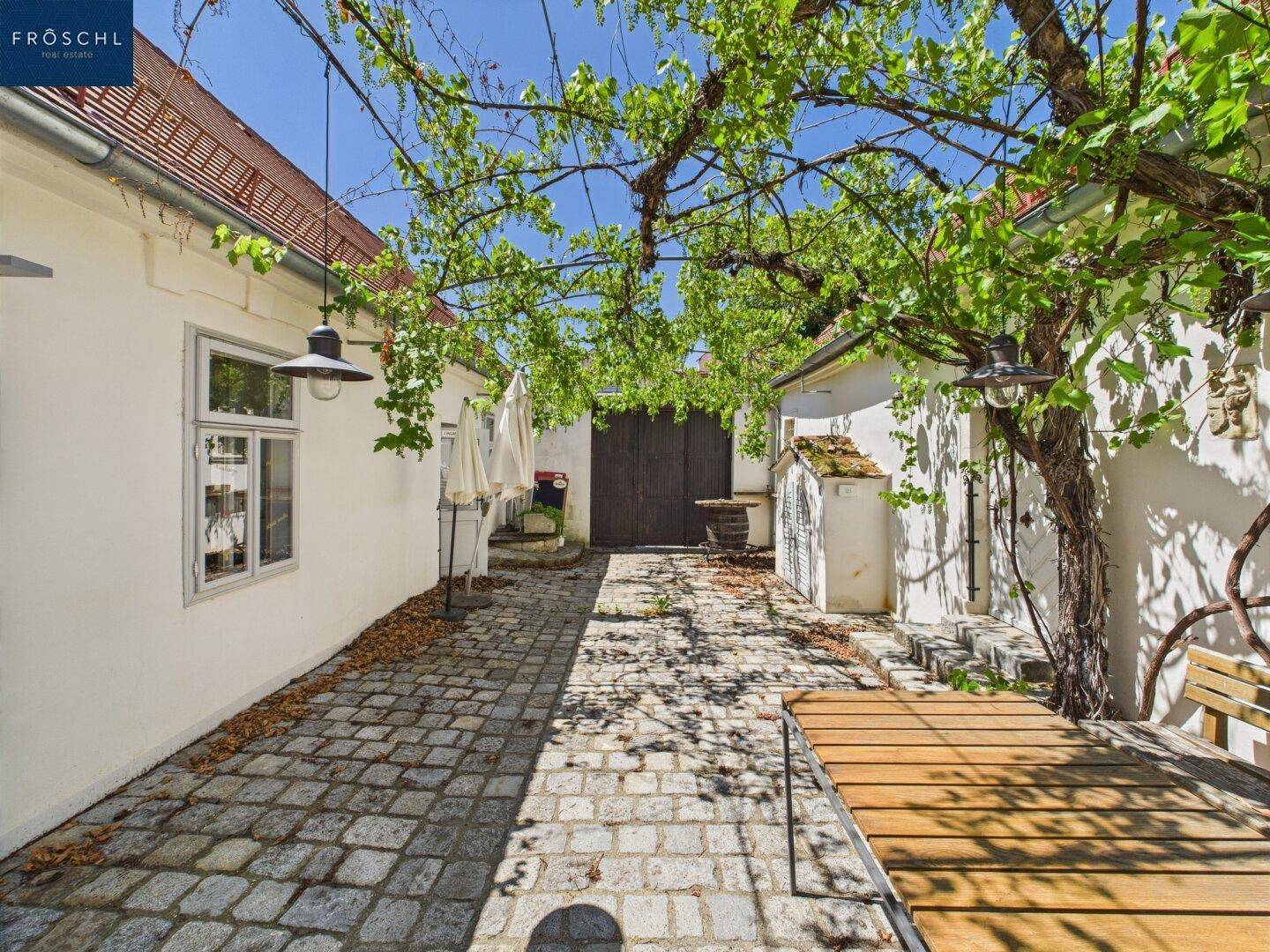 Gemütlicher Innenhof mit Weinreben, die Schatten spenden, und rustikalen Holztischen für Gäste.