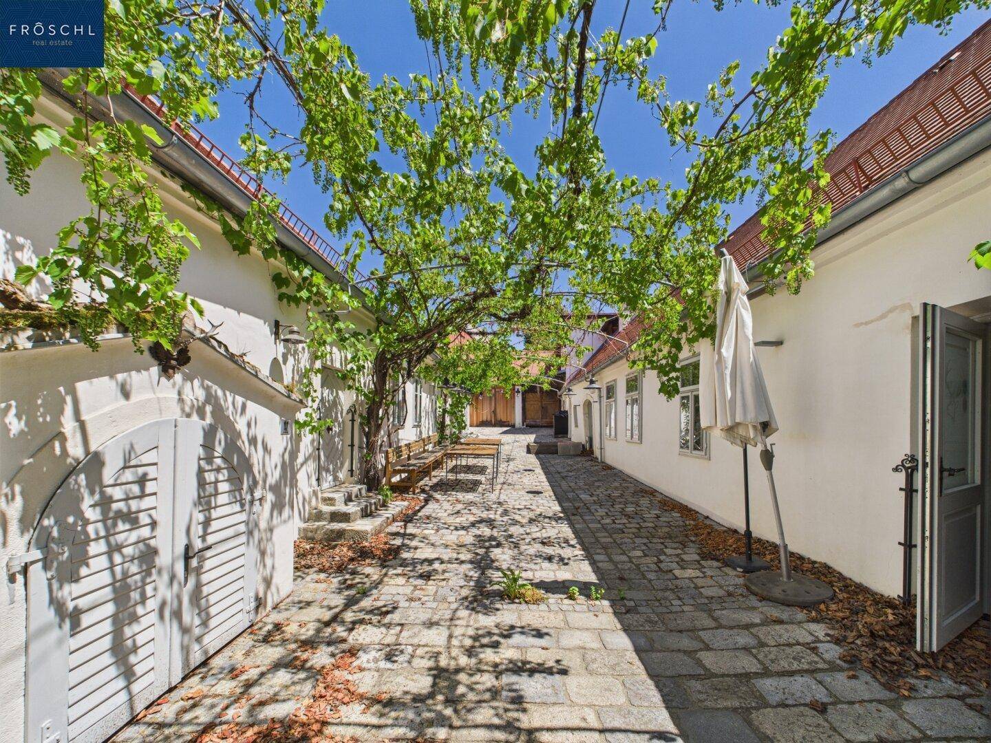 Malerischer Innenhof mit Kopfsteinpflaster und üppigem Weinlaub, das Schatten spendet.