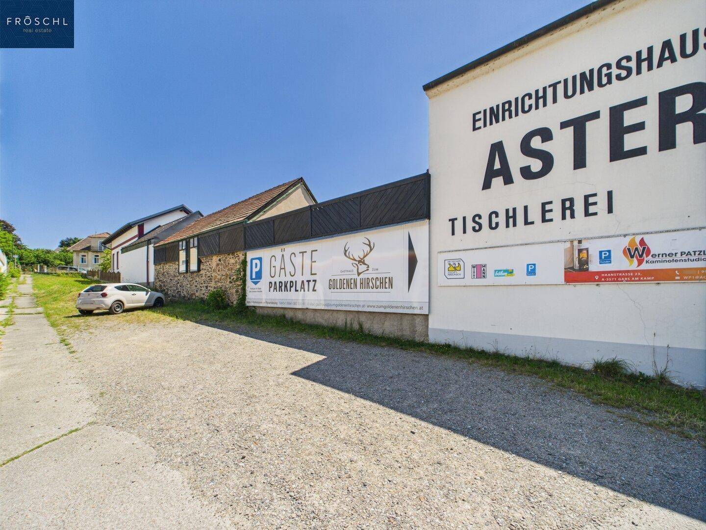 Gebäude mit großer Werbetafel und Parkplatz für Gäste, an einer Straße gelegen.