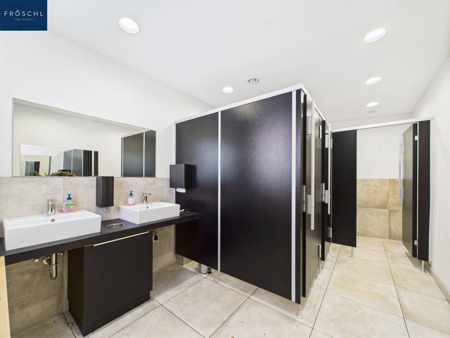 Moderne und saubere Toilettenanlage mit Doppelwaschbecken und schwarzen Trennwänden.