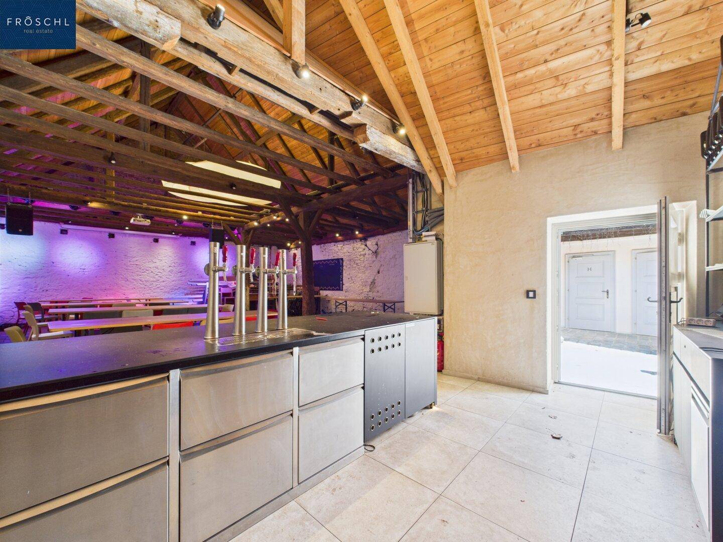 Großer Veranstaltungsraum mit offener Holzdachkonstruktion und moderner Bar.