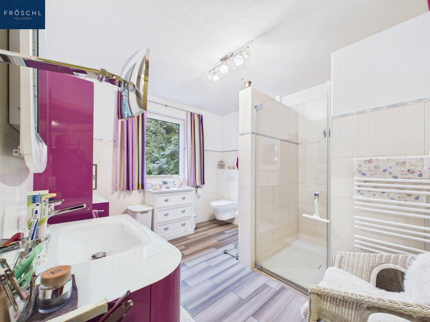 Modernes Badezimmer mit lila Akzenten, ebenerdiger Dusche und Fenster für natürliches Licht.