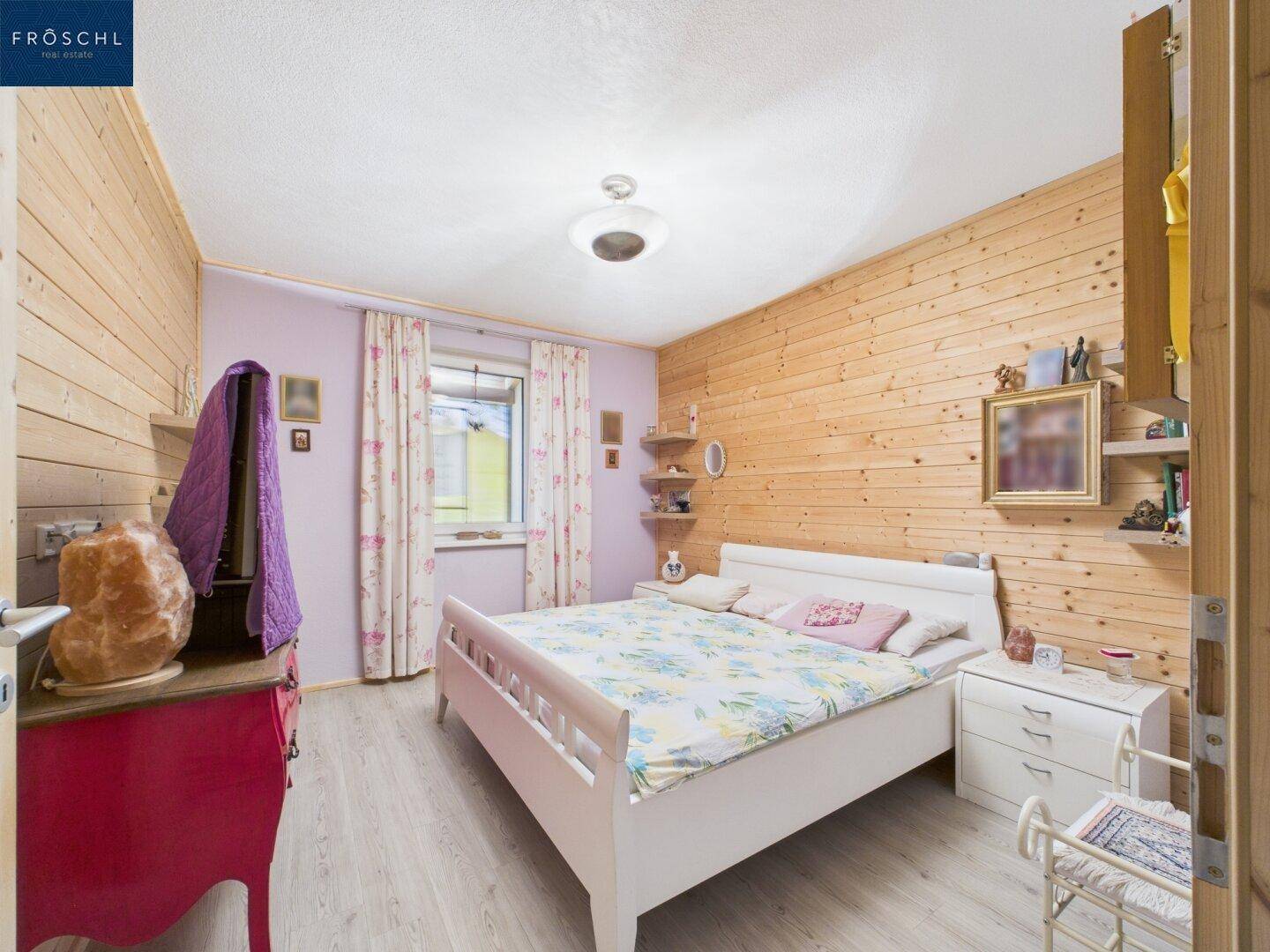 Helles Schlafzimmer mit Holzwänden, Doppelbett und Fenster mit Blick ins Grüne.