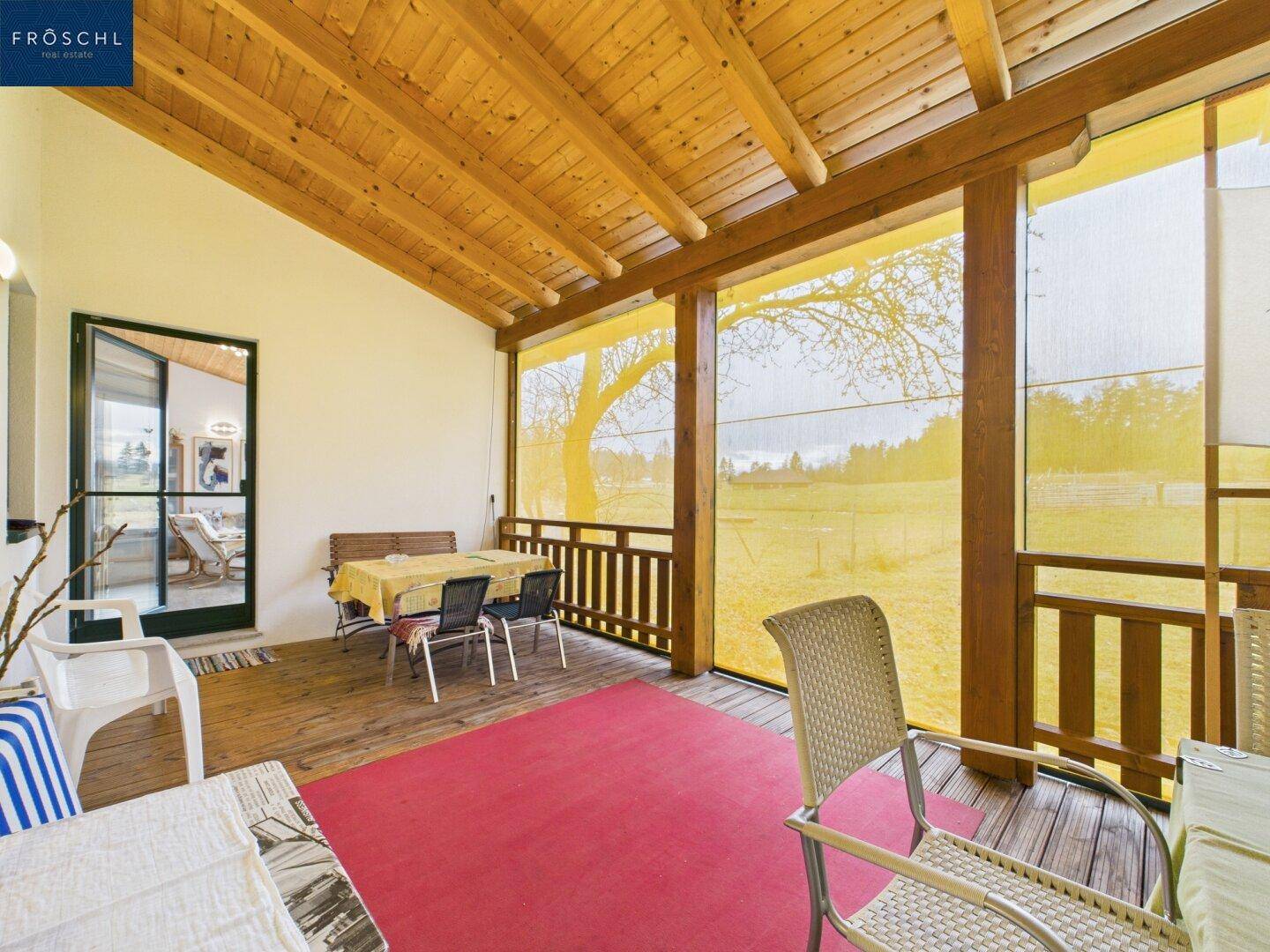 Überdachte Loggia mit Holzboden, Esstisch und Blick auf die umliegende Natur.