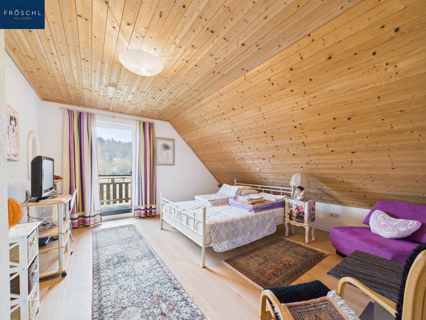 Schlafzimmer im Dachgeschoss mit Holzdachschrägen, Doppelbett und Zugang zum Balkon.