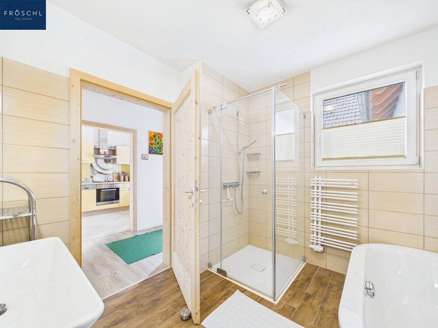 Badezimmer mit Dusche, Badewanne und Fenster, angrenzend an die gelbe Küche.
