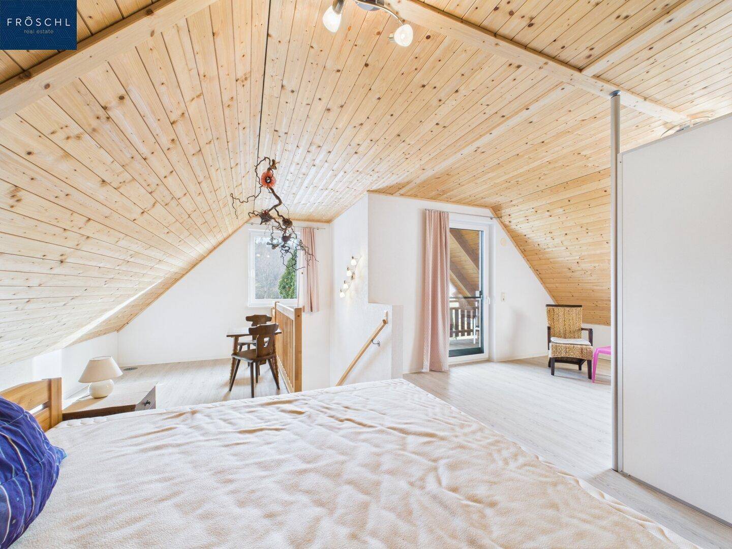 Geräumiges Schlafzimmer im Dachgeschoss mit Holzdachschrägen und Zugang zu einem Balkon.
