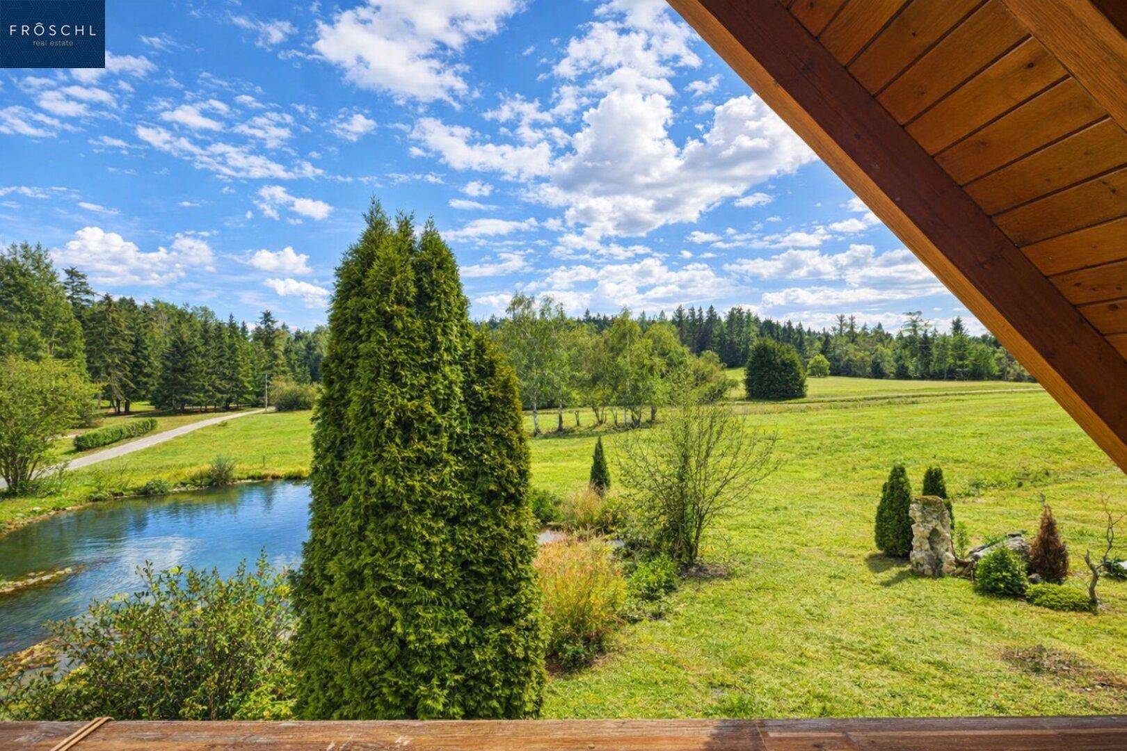 Malerischer Ausblick von einem Balkon über einen Teich und weite grüne Felder.