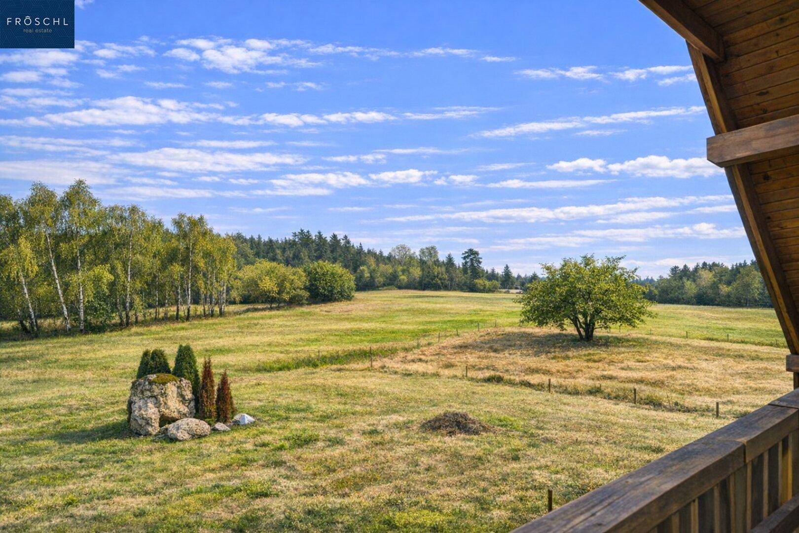 Weitläufiger Ausblick von einem Balkon über grüne Felder und bewaldete Hügel.