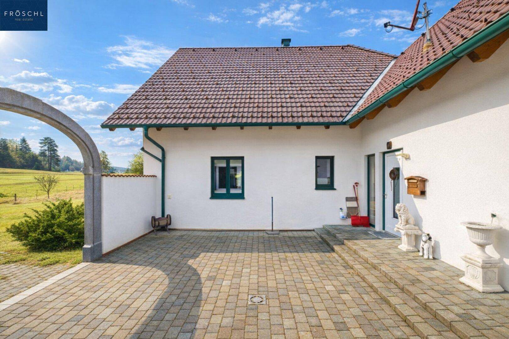 Gepflasterter Hofbereich mit Zugang zum Haus und Blick auf die grüne Landschaft.