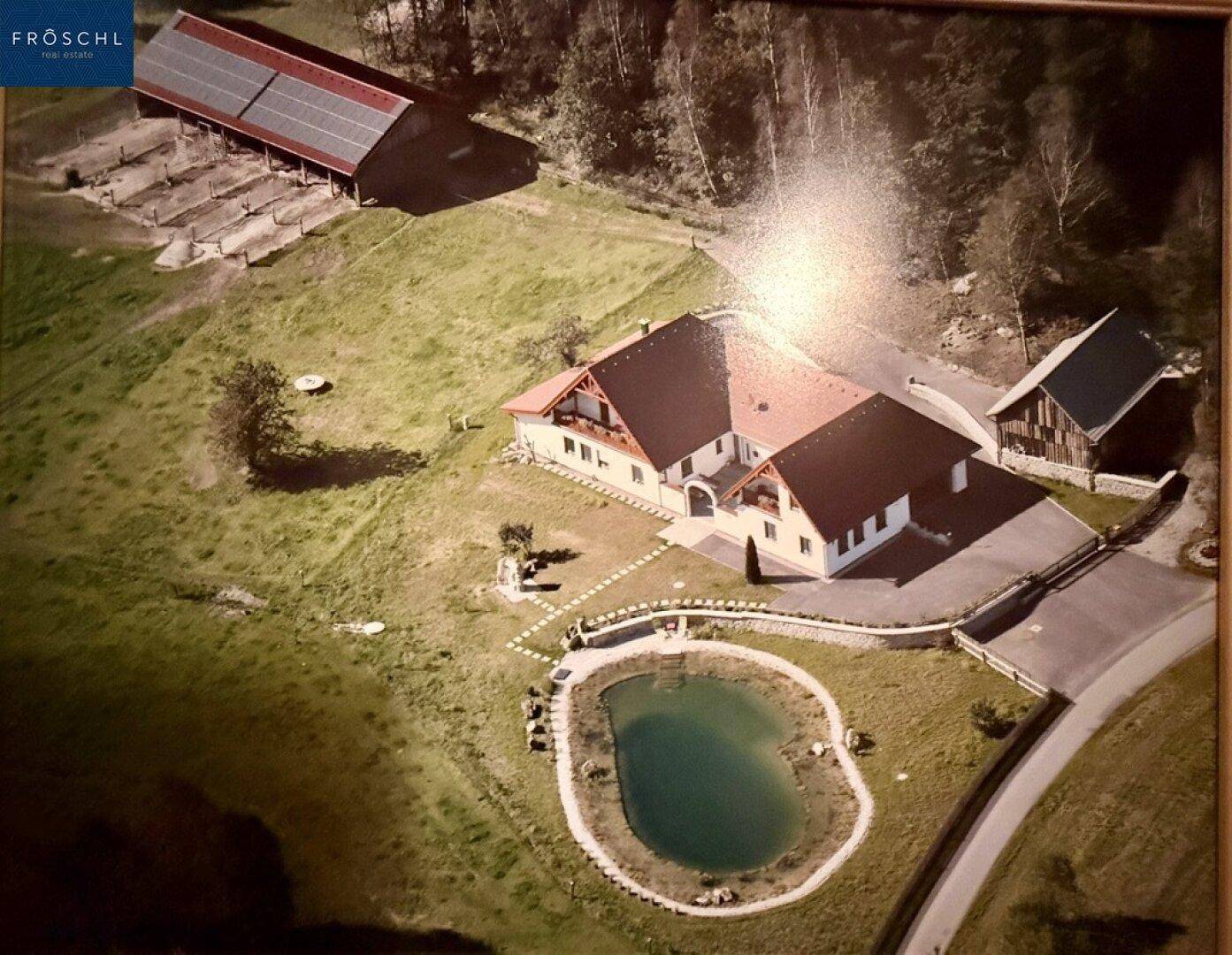 Luftaufnahme eines Anwesens mit Haupthaus, Teich und Scheune mit Photovoltaikanlage.
