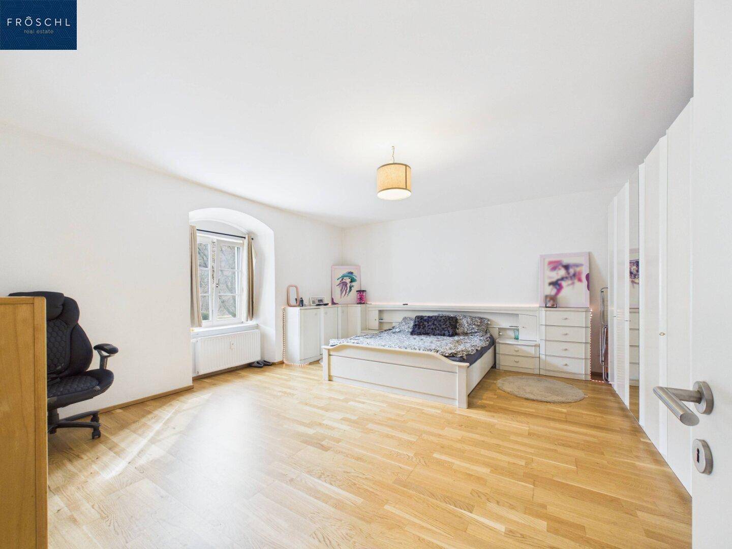 Schlafzimmer mit integrierten Schränken, Holzboden und Fenster für natürliches Licht.