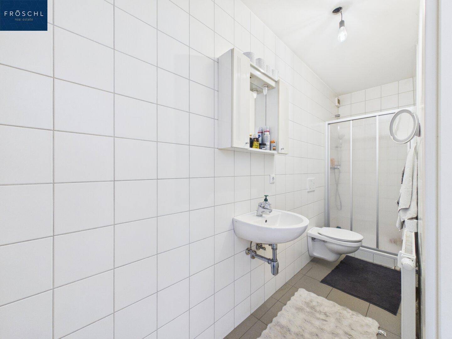 Modernes Badezimmer mit weißen Fliesen, Dusche, Waschbecken und Toilette.