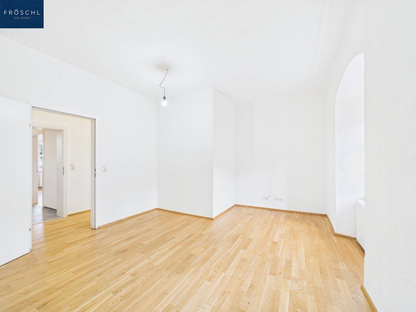 Heller Raum mit Holzboden und weiß gestrichenen Wänden, ideal als Wohnzimmer.