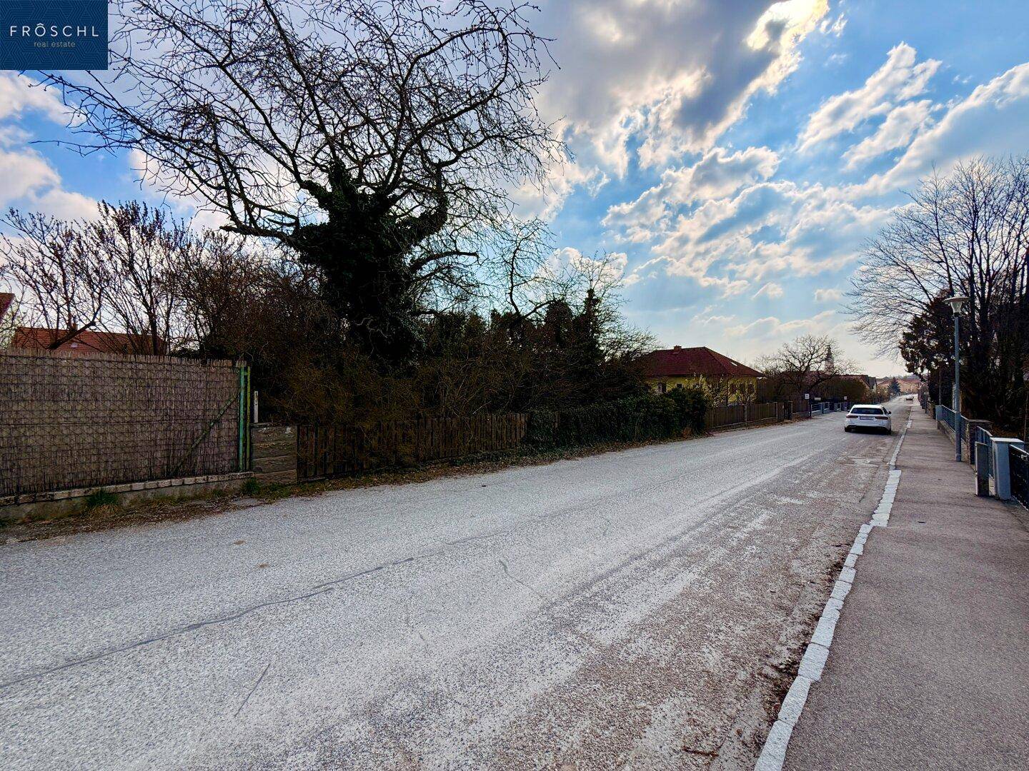 Ländliche Straße mit parkendem Auto und Blick auf die umliegende Wohnbebauung.