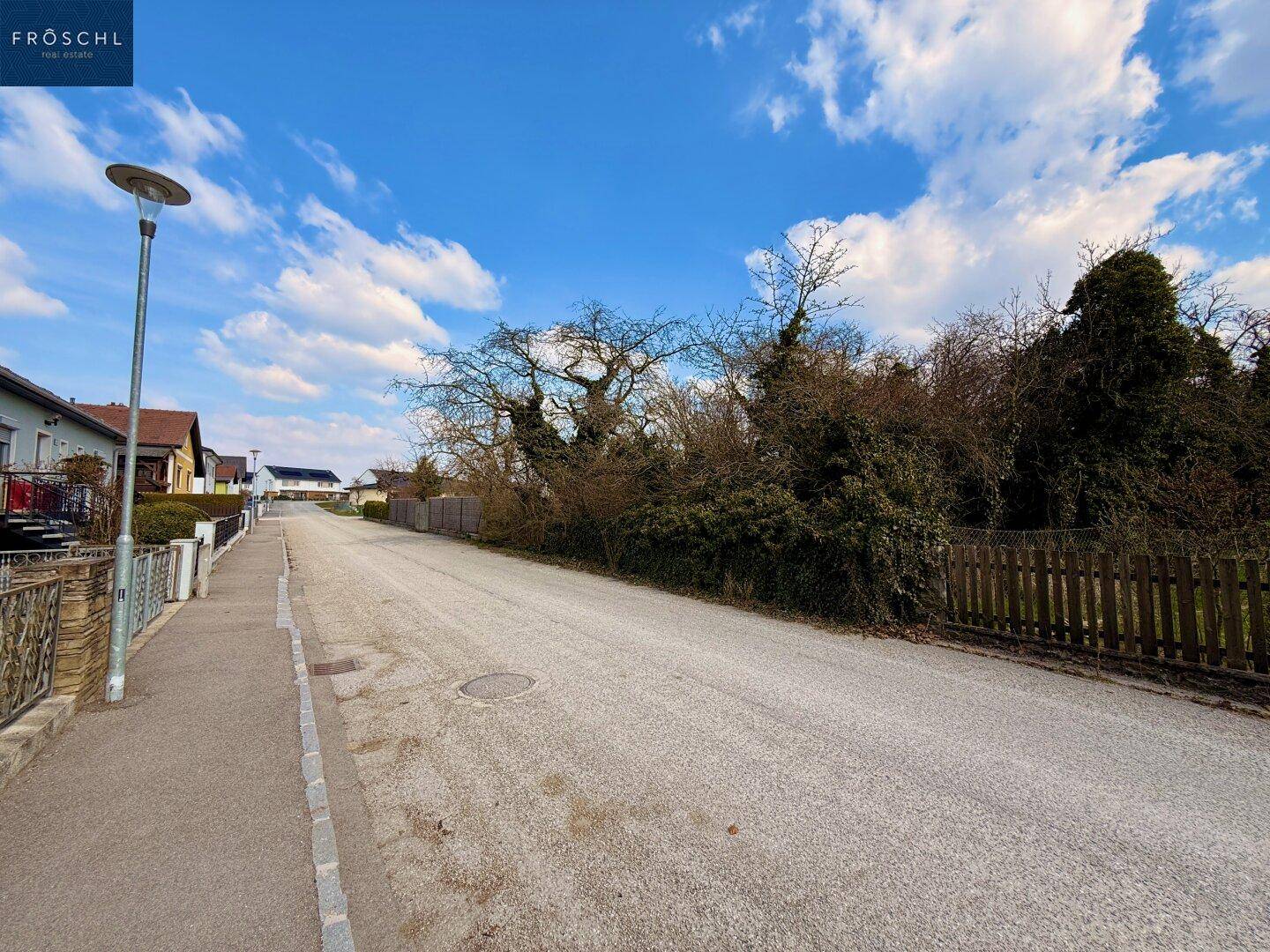 Blick entlang der ruhigen Wohnstraße mit angrenzendem Grundstück und Laterne.