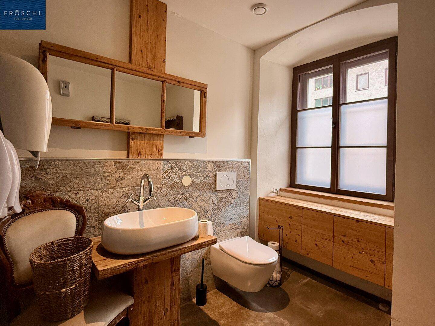 Modernes Badezimmer mit ovalem Waschbecken, Holzmöbeln und Fenster.