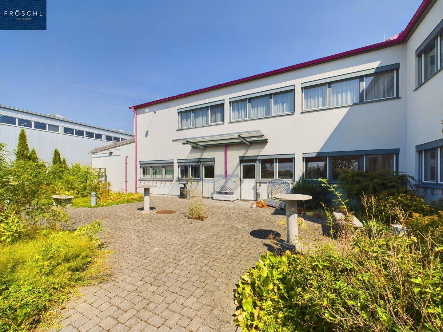 Gepflasterter Innenhof mit Grünflächen, Sitzgelegenheiten und der Gebäudefassade im Hintergrund.