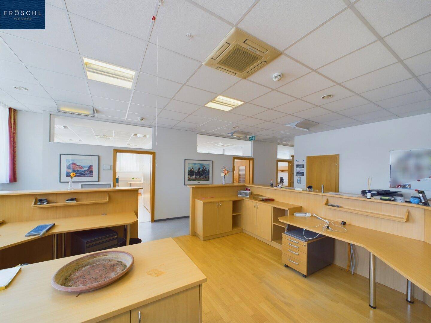 Empfangsbereich oder offenes Büro mit Holzschreibtischen und Durchgängen zu weiteren Büroräumen.