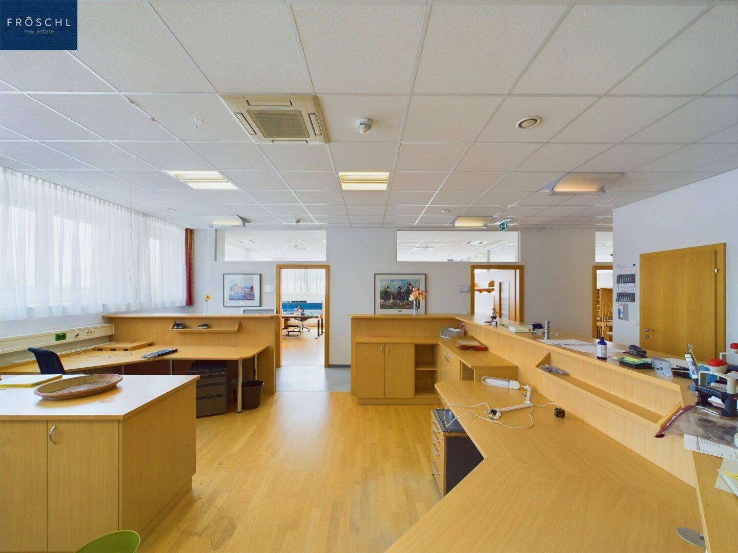 Geräumiger Empfangsbereich oder offenes Büro mit mehreren Arbeitsplätzen und hellem Holzfußboden.