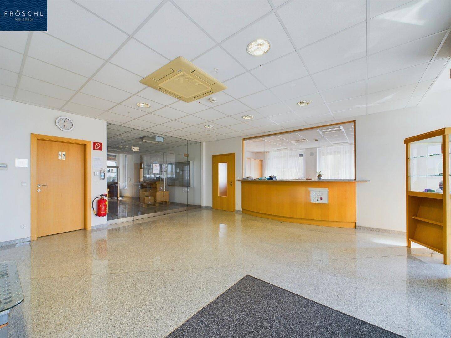 Geräumiger Empfangsbereich mit heller Einrichtung, glänzendem Boden und Zugang zu weiteren Büroräumen.