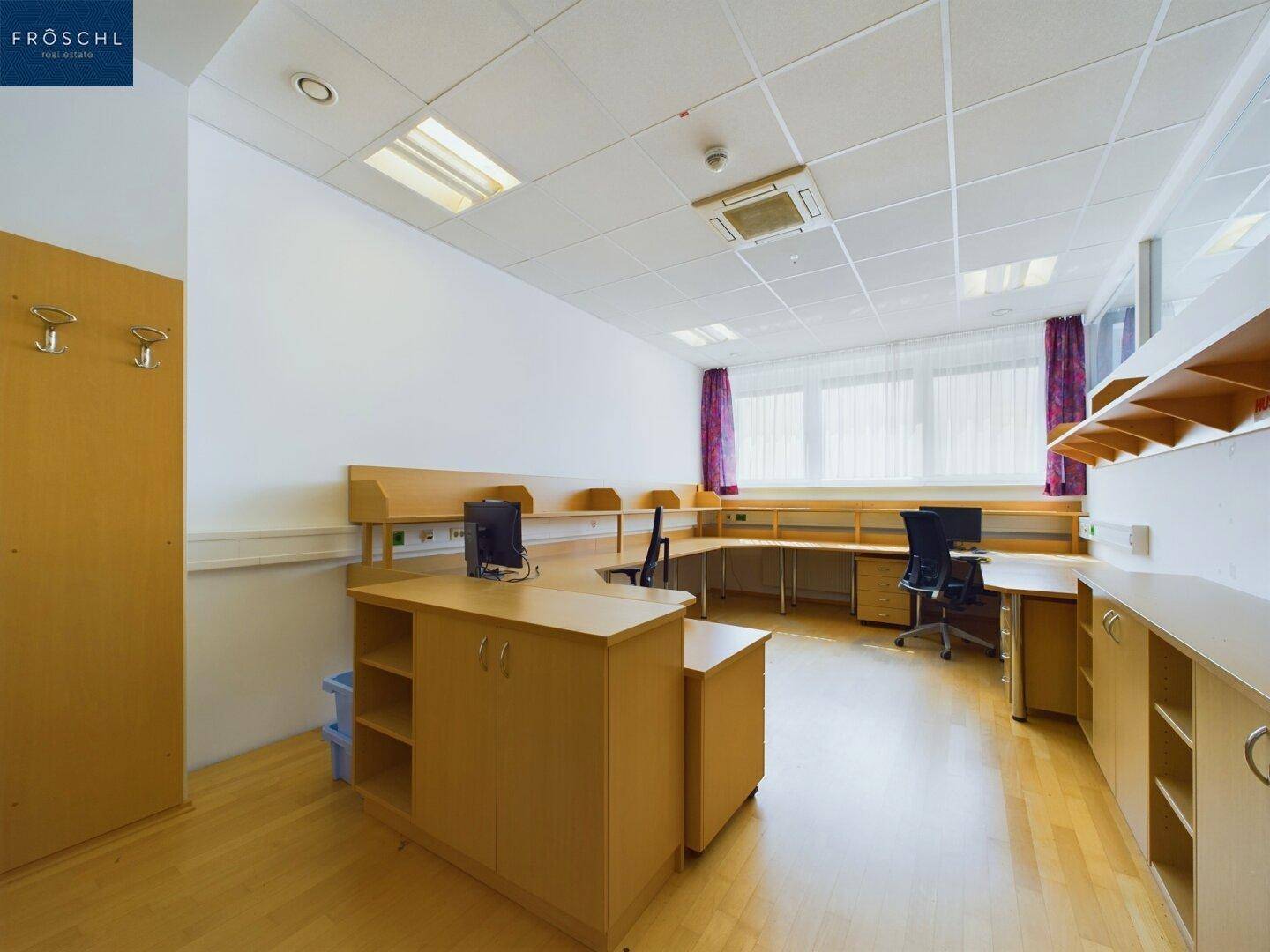 Helles Büro mit mehreren Arbeitsplätzen, Holzfußboden und großen Fenstern für viel Tageslicht.