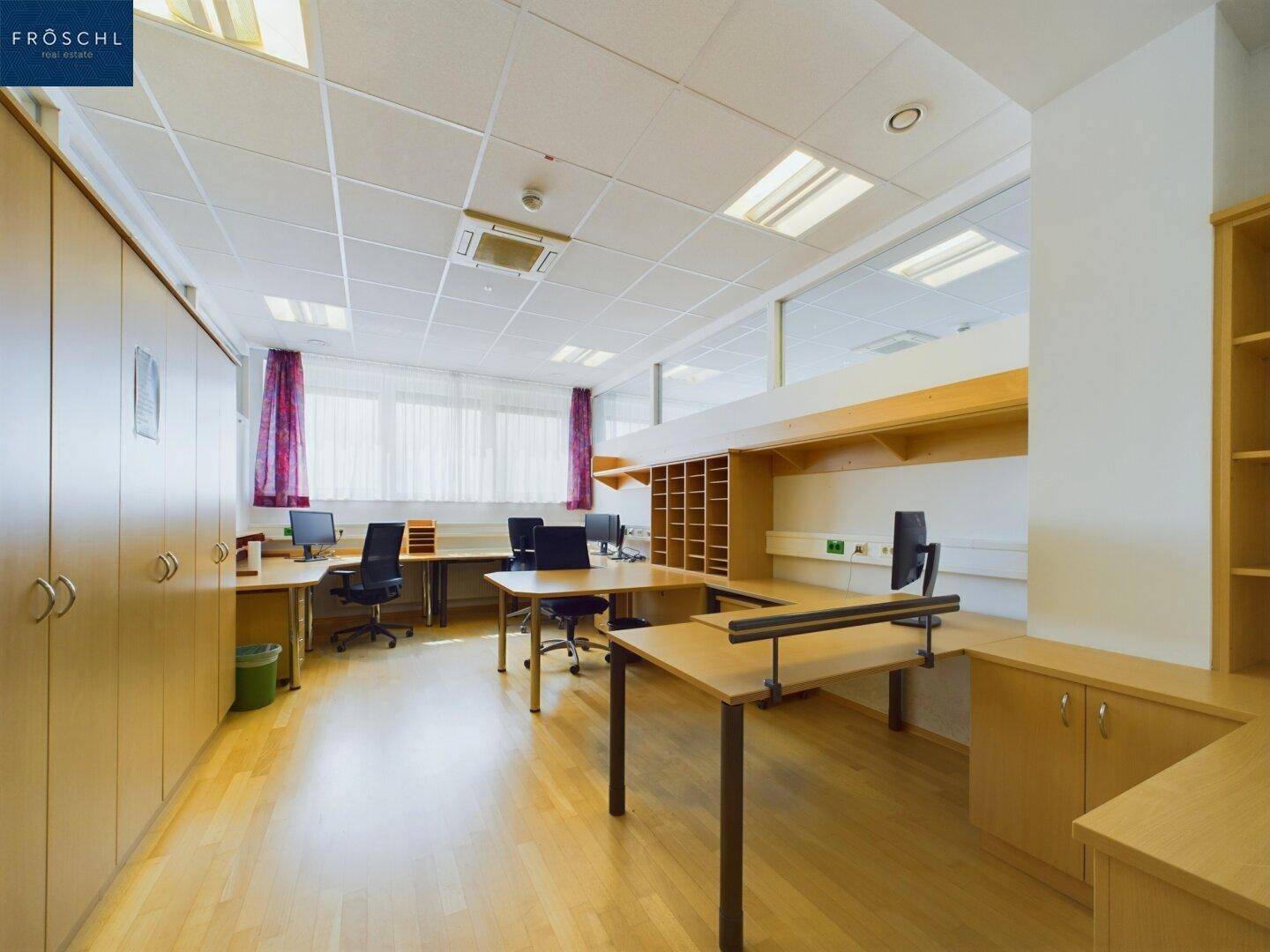 Geräumiges Büro mit mehreren Schreibtischen, Holzfußboden und integrierten Schränken für Stauraum.